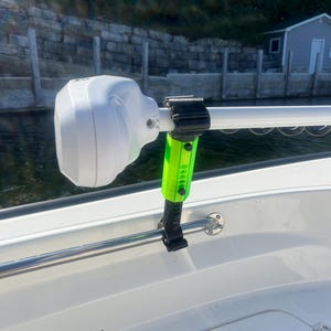 Puede incluir: Un soporte de barco blanco y negro con un brazo de extensi&oacute;n verde y negro. El soporte est&aacute; unido a una barandilla plateada en un barco.