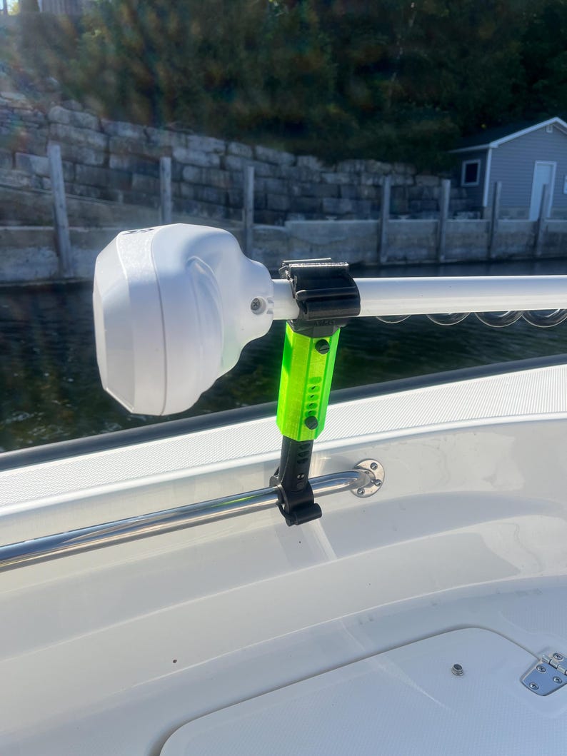 Puede incluir: Un soporte de barco blanco y negro con un brazo de extensi&oacute;n verde y negro. El soporte est&aacute; unido a una barandilla plateada en un barco.