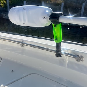 Puede incluir: Un motor de barco blanco con un soporte verde y negro. El motor est&aacute; unido a un barco blanco.