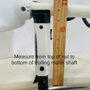 Puede incluir: Un soporte de motor de pesca de arrastre blanco con un soporte negro y una regla que mide 17,8 cm. El texto "Measure from top of rail to bottom of trolling motor shaft" es visible en la imagen.