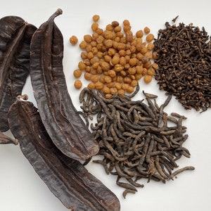 Peut inclure: Une collection d'herbes et d'épices séchées, y compris des gousses de caroube, des grains de poivre bruns et jaunes et des clous de girofle bruns.