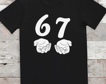 May include: Black t-shirt with a white graphic. The graphic features the number "67" above two stylized open hands. The design is centered on the shirt, making it a simple yet eye-catching piece.