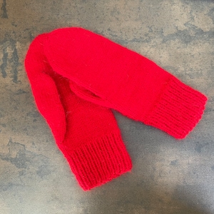 May include: A pair of red knitted mittens. The mittens are made from a soft, warm yarn and have a simple, classic design.