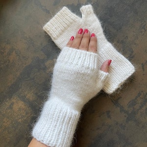 May include: White fingerless gloves with a fuzzy texture. The gloves have a long cuff and are made of a soft, knitted fabric.