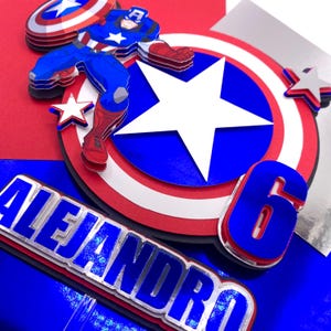 Puede incluir: Adorno para tarta en capas con tem&aacute;tica de Capit&aacute;n Am&eacute;rica, en colores azul, rojo y blanco. El dise&ntilde;o incluye una figura del Capit&aacute;n Am&eacute;rica, un escudo, estrellas, el n&uacute;mero 6 y el nombre "Alejandro".