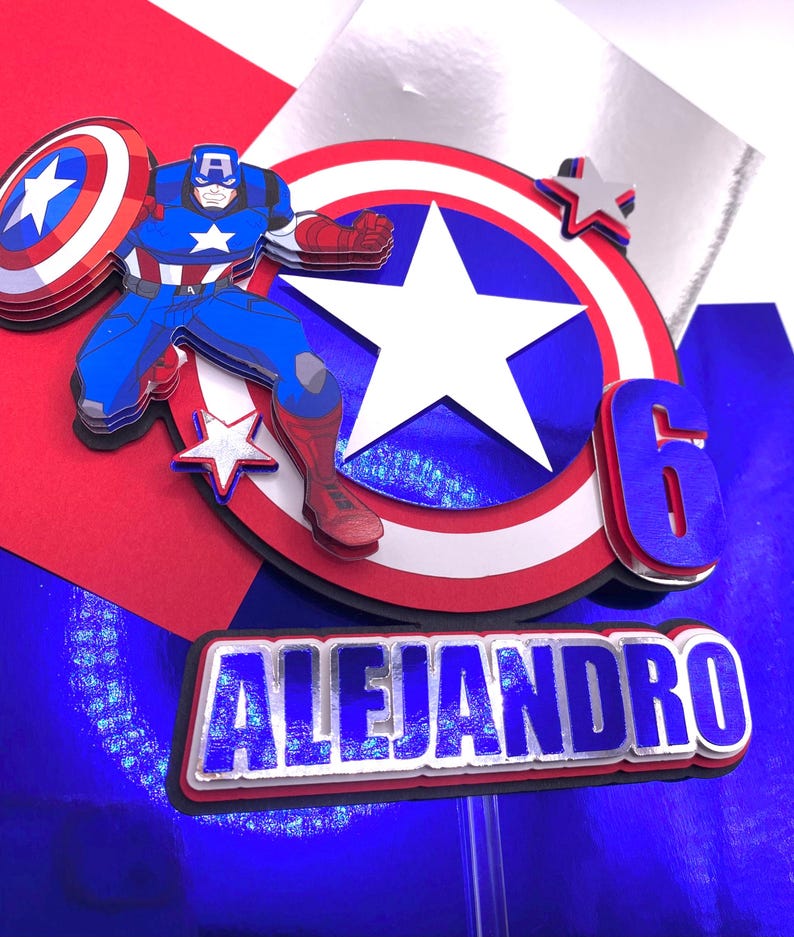 Puede incluir: Adorno para tarta de varias capas con el Capit&aacute;n Am&eacute;rica con su escudo, una gran estrella y el n&uacute;mero 6. El nombre "ALEJANDRO" se muestra debajo. El dise&ntilde;o incorpora los colores rojo, blanco, azul y plateado, ideal para una fiesta de cumplea&ntilde;os.