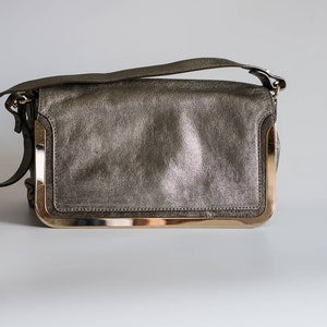 May include: A metallic gray leather shoulder bag with a gold-toned frame and a strap.