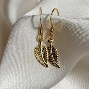 May include: A pair of gold leaf dangle earrings. The earrings are made of thin gold wire and have a delicate leaf design.