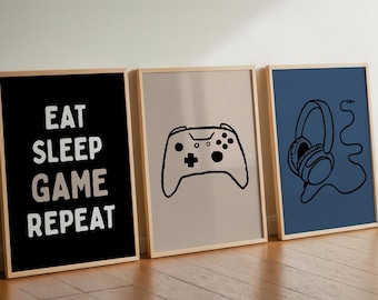 Op de afbeelding: Drie ingelijste kunstprints met een gaming thema. De eerste print heeft de tekst "EAT SLEEP GAME REPEAT" op een zwarte achtergrond. De tweede print toont een zwarte omtrek van een gamecontroller op een beige achtergrond. De derde print toont een zwarte omtrek van een koptelefoon op een blauwe achtergrond.