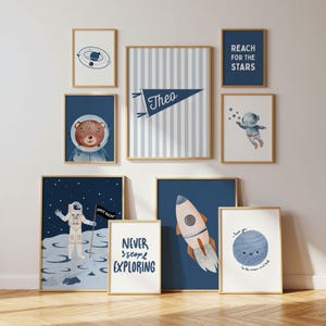 May include: A gallery wall set of nine framed prints featuring space-themed illustrations including an astronaut, a rocket, a bear in a helmet, and planets. Text includes "REACH FOR THE STARS", "NEVER stop EXPLORING", "Theo", and "I love you to the moon and back".