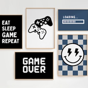 Peut inclure: Un ensemble de cinq cadres muraux sur le thème du jeu vidéo. Comprend des affiches noires avec le texte blanc EAT SLEEP GAME REPEAT et GAME OVER, une affiche blanche avec des manettes noires, une bleue avec LOADING et un visage souriant à damier.