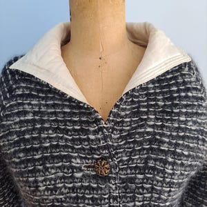 May include: A vintage black and white textured jacket with a cream-colored collar. The jacket features decorative bronze-colored buttons. The jacket is displayed on a mannequin.