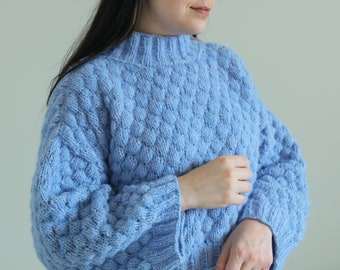 May include: A light blue knitted jumper with a textured pattern. The jumper has a high neck and long sleeves.