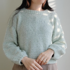 Könnte beinhalten: Ein hellblauer Strickpullover mit einem strukturierten Muster. Der Pullover hat einen runden Ausschnitt und lange Ärmel.