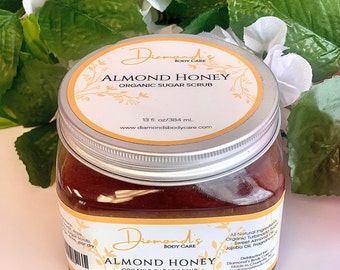 May include: A glass jar with a silver lid containing a brown sugar scrub. The label reads "Diamond's Body Care Almond Honey Organic Sugar Scrub 13 fl. oz/384 mL www.diamondsbodycare.com".