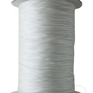May include: A large spool of white cord. The cord is tightly wound around a cardboard core. The spool is cylindrical with a flat top and bottom. The cord appears to be made of a smooth, synthetic material. The background is plain white.