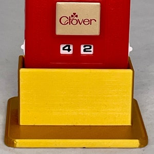 May include: Red plastic Clover brand sewing machine needle threader with a yellow base and a number display showing 42.