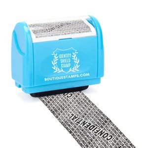 May include: A light blue identity shield stamp with the text "CONFIDENTIAL" printed repeatedly on a black strip. The stamp has the text "IDENTITY SHIELD STAMP" and "BOUTIQUESTAMPS.COM".