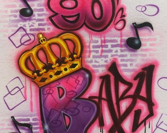May include: A white t-shirt with a pink and purple graffiti design. The design includes the number 90's, a crown, and the word "BABA".
