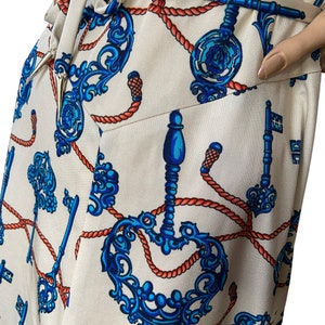 May include: A white wrap dress with a blue and orange pattern of ornate keys and rope. The dress has a self-tie belt.