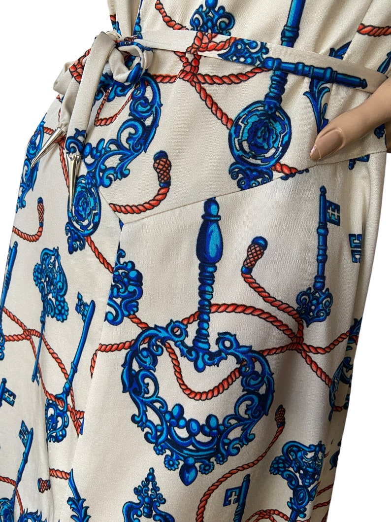 May include: A white wrap dress with a blue and orange pattern of ornate keys and rope. The dress has a self-tie belt.