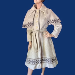 May include: A vintage beige coat with a matching belt and brown geometric patterns. The coat has a cape-like design over the shoulders and is buttoned down the front. The coat is displayed on a mannequin.