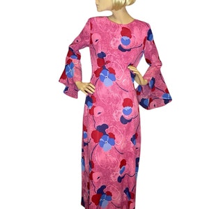 May include: A long pink maxi dress with a floral print featuring blue, red, and pink flowers. The dress has long bell sleeves and a round neckline.