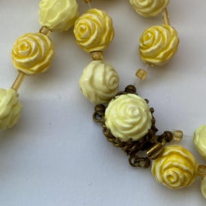 May include: A vintage necklace featuring rose-shaped beads in shades of yellow and cream. The beads are strung together with a delicate chain and clasp. The necklace has a classic, feminine design.