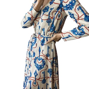 May include: A cream-colored dress with a long sleeve and a V-neck. The dress has a blue and red pattern of keys and rope.