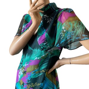 May include: A green, blue, pink and gold abstract print dress with a high neck and short sleeves.