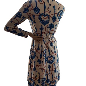 May include: A white dress with a blue and red key pattern. The dress has long sleeves and a fitted bodice. The skirt is a-line and falls to the knees.