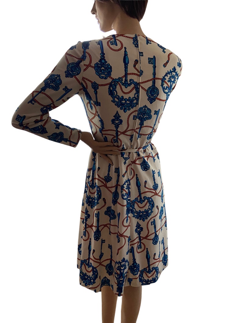 May include: A white dress with a blue and red key pattern. The dress has long sleeves and a fitted bodice. The skirt is a-line and falls to the knees.