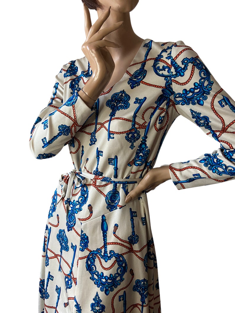 May include: A long-sleeved wrap dress with a V-neckline. The dress is made of a white fabric with a pattern of blue keys and red rope.