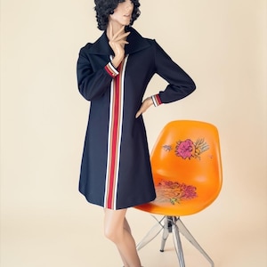 May include: A navy blue dress with a white, red, and tan stripe down the front. The dress has long sleeves with striped cuffs. An orange chair with a floral design is next to the dress.