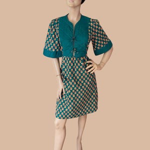 May include: A knee-length dress featuring a dark green quilted bodice with a front tie closure and short sleeves. The lower portion of the dress and the sleeves are patterned with small orange and yellow floral motifs on a dark green background.