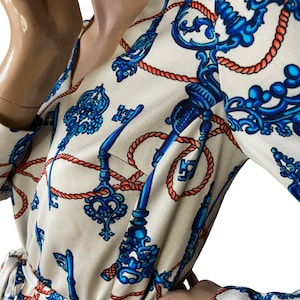May include: A white dress with a long sleeve and a V-neck. The dress has a pattern of blue keys and red rope.