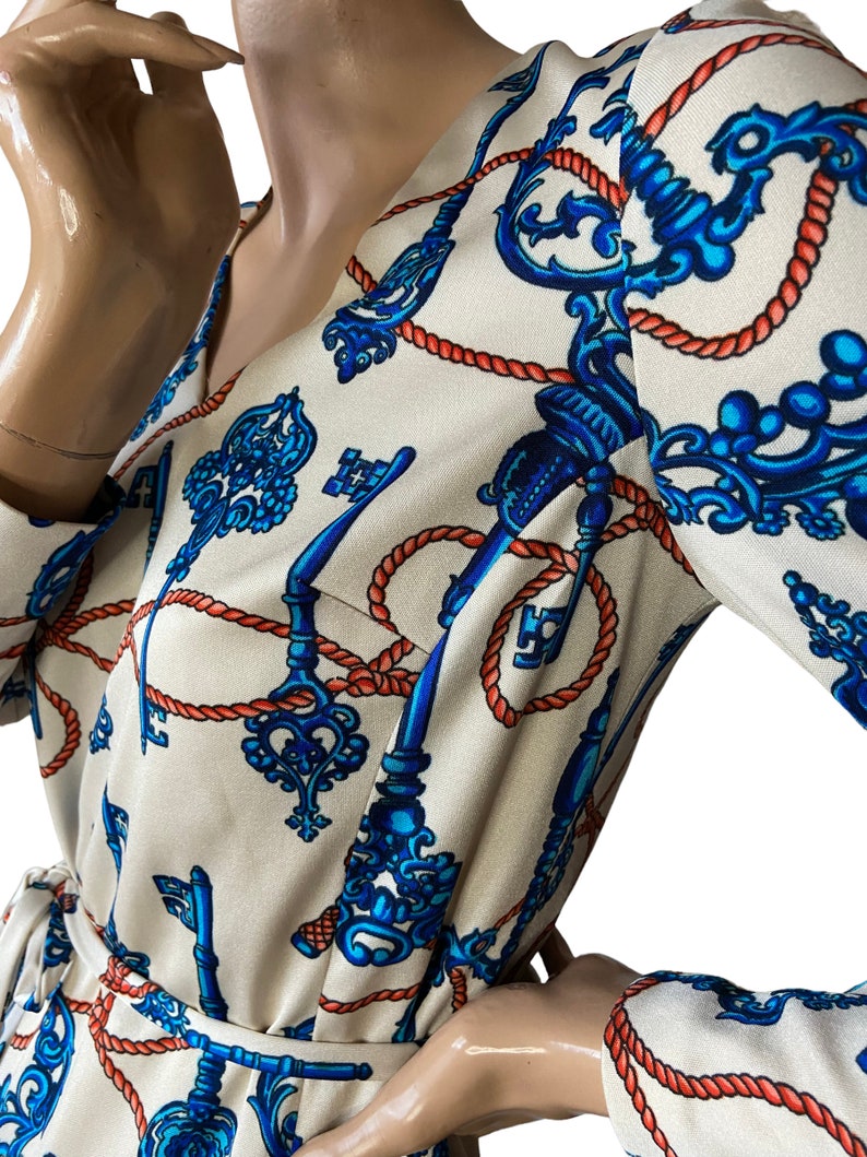May include: A white dress with a long sleeve and a V-neck. The dress has a pattern of blue keys and red rope.