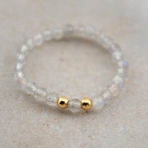 Könnte beinhalten: Ein zartes Armband aus kleinen, klaren, schillernden Perlen mit zwei goldenen Perlen in der Mitte.