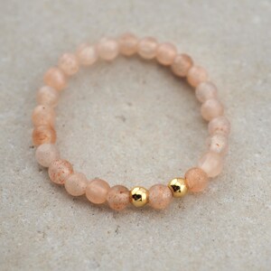 Könnte beinhalten: Ein zartes Armband aus kleinen, hellrosa Perlen mit goldenen Akzenten. Das Armband ist aus natürlichen Steinen gefertigt und perfekt für den täglichen Gebrauch.