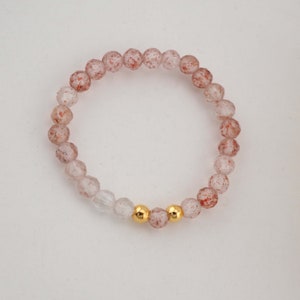 Könnte beinhalten: Ein zartes Armband aus klaren und rotbraunen facettierten Perlen, akzentuiert mit zwei goldenen Perlen.