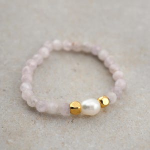 Könnte beinhalten: Ein zartes Armband aus kleinen rosa Perlen mit einem einzelnen Perlenakzent. Das Armband ist mit zwei goldenen Perlen verziert.