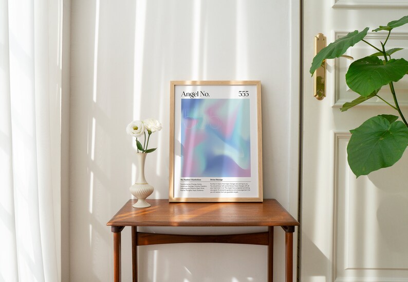 May include: A framed print with a light blue, pink, and purple abstract design. The print has the text "Angel No. 555" at the top.