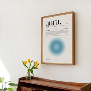 May include: A framed print with the word "aura." in black text on a white background. The print also features a blue circle with a gradient effect. The print is hanging on a white wall.