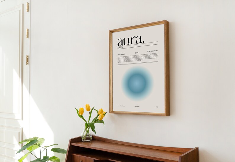 May include: A framed print with the word "aura." in black text on a white background. The print also features a blue circle with a gradient effect. The print is hanging on a white wall.