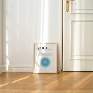 May include: A framed print with the word "aura." in black text on a white background. The print features a blue and white gradient circle in the center.