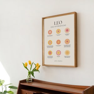 May include: A framed print with a light beige background and the text "LEO DAILY AFFIRMATIONS" in black. The print features nine circles with different shades of pink and yellow, each with a short affirmation written in black text. The bottom of the print reads "JULY 23 - AUGUST 22".