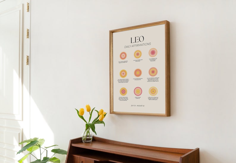 May include: A framed print with a light beige background and the text "LEO DAILY AFFIRMATIONS" in black. The print features nine circles with different shades of pink and yellow, each with a short affirmation written in black text. The bottom of the print reads "JULY 23 - AUGUST 22".
