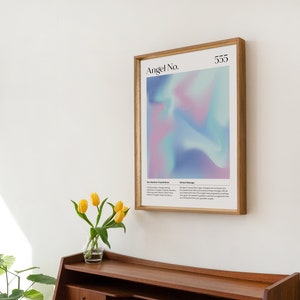 May include: A framed print with a light blue, pink, and purple gradient background. The print has the text "Angel No. 555" at the top. The print is in a wooden frame.