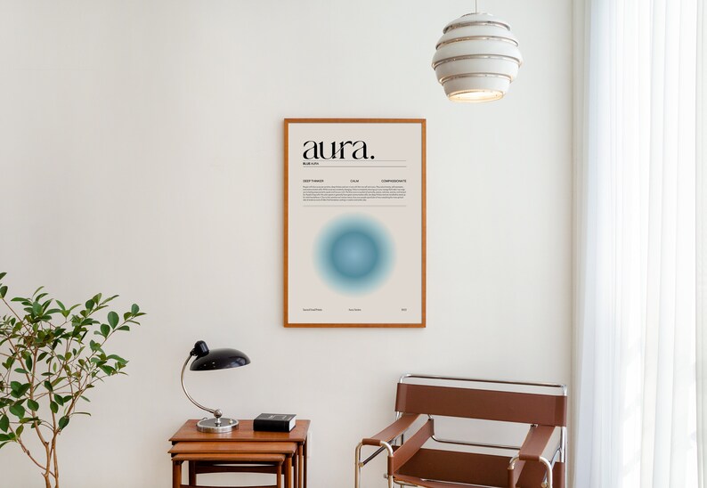 May include: A framed poster with the word "aura" in black text on a light beige background. The poster features a blue circle with a gradient effect and text about the color blue. The poster is hanging on a white wall.