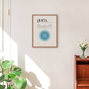 May include: A framed print with the word "aura" in black text on a white background. The print features a blue and green gradient circle in the center. The print is hanging on a white wall.